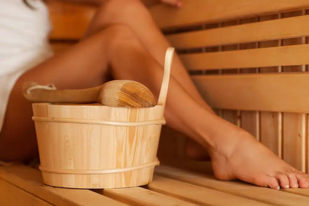Femme profitant d’un moment de détente dans un sauna en bois avec un seau et une louche